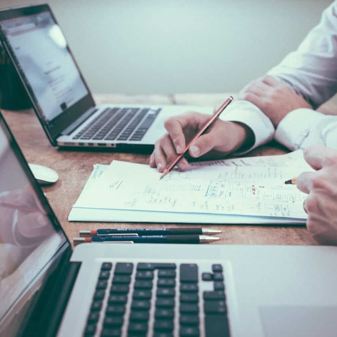 dos personas usando ordenadores y haciendo anotaciones en un documento escrito