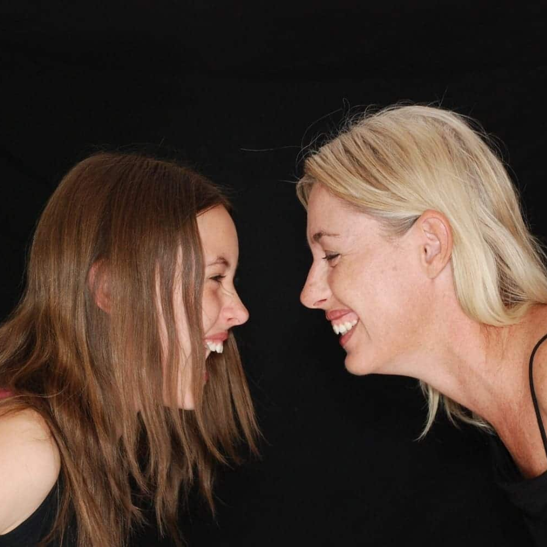 dos mujeres enfrente la una de la otra, ambas sonriendo y con el cuello y cabeza hacia adelante