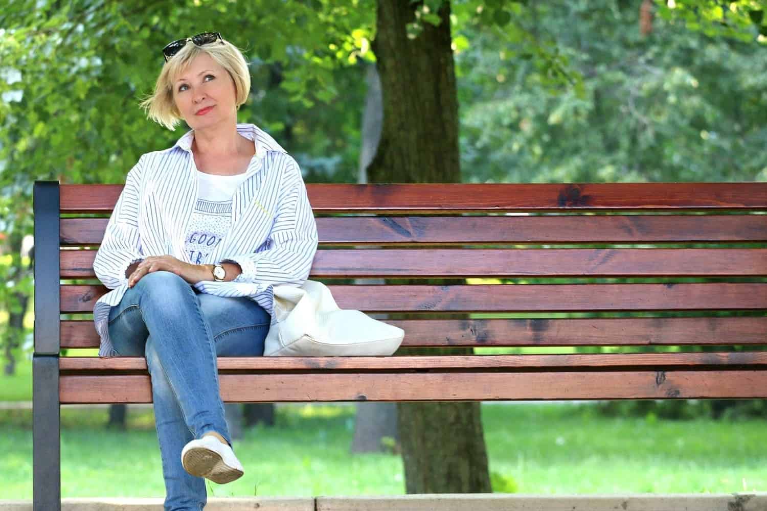 una mujer sentada en una banca en medio de la naturaleza, mientras mira hacia un lugar determinado