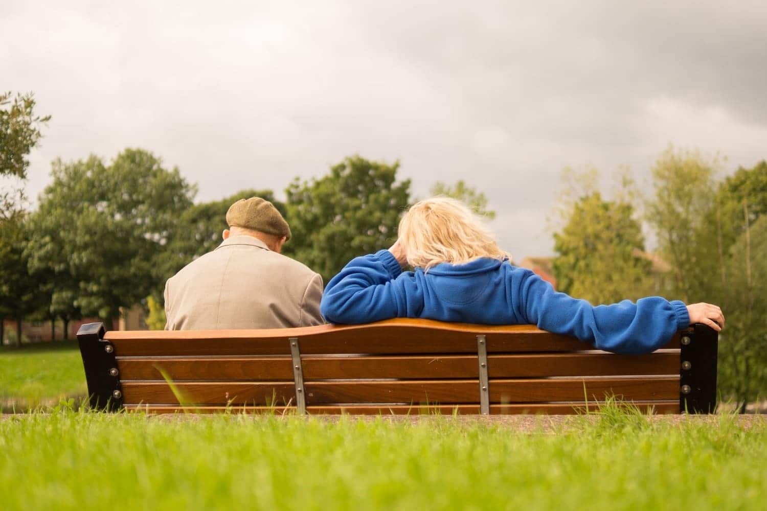 dos adultos mayores sentados en una banca en medio de un parque