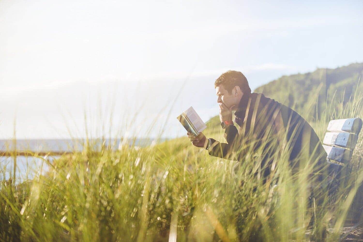 un hombre leyendo en una banca que da la vista a un cuerpo de agua, la imagen denota relajación