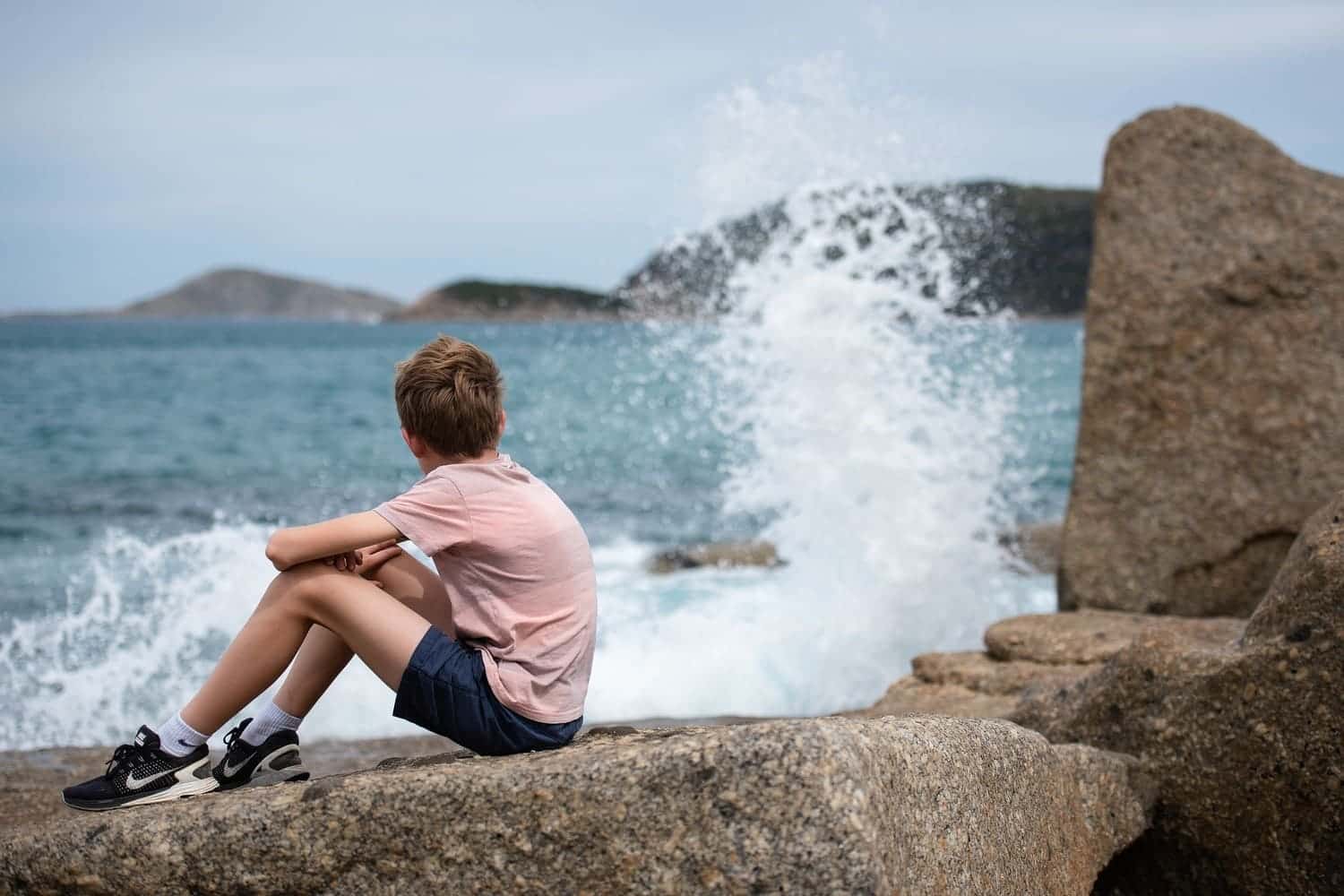 un niño sentando en una roca a la orilla de la playa