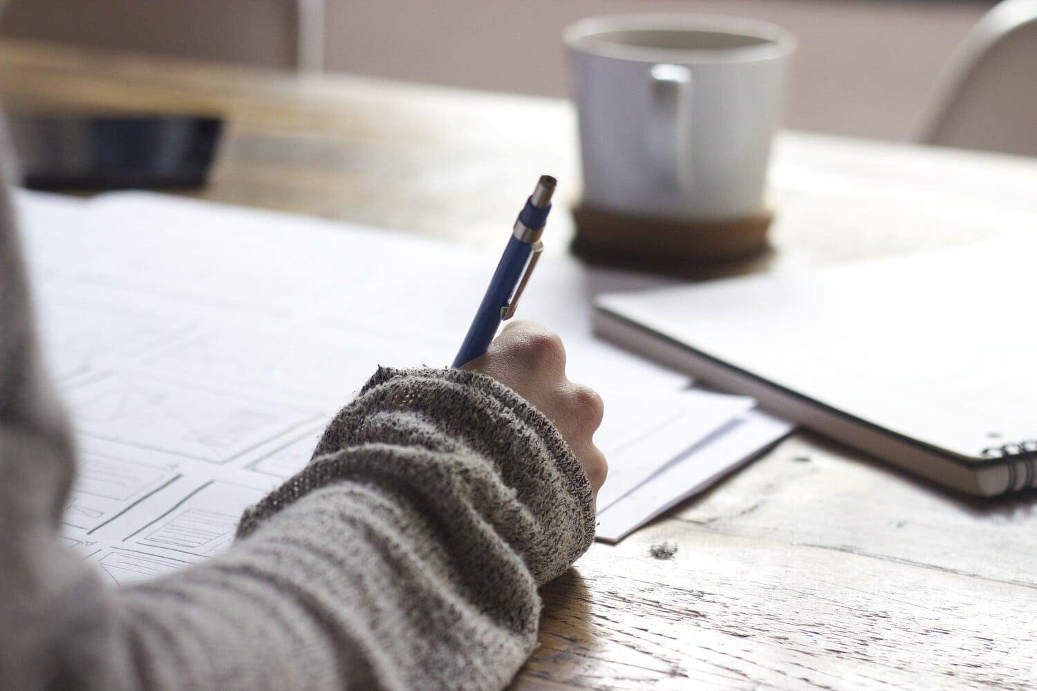 un adulto escribiendo, alrededor se logran ver más documentos y una taza de café