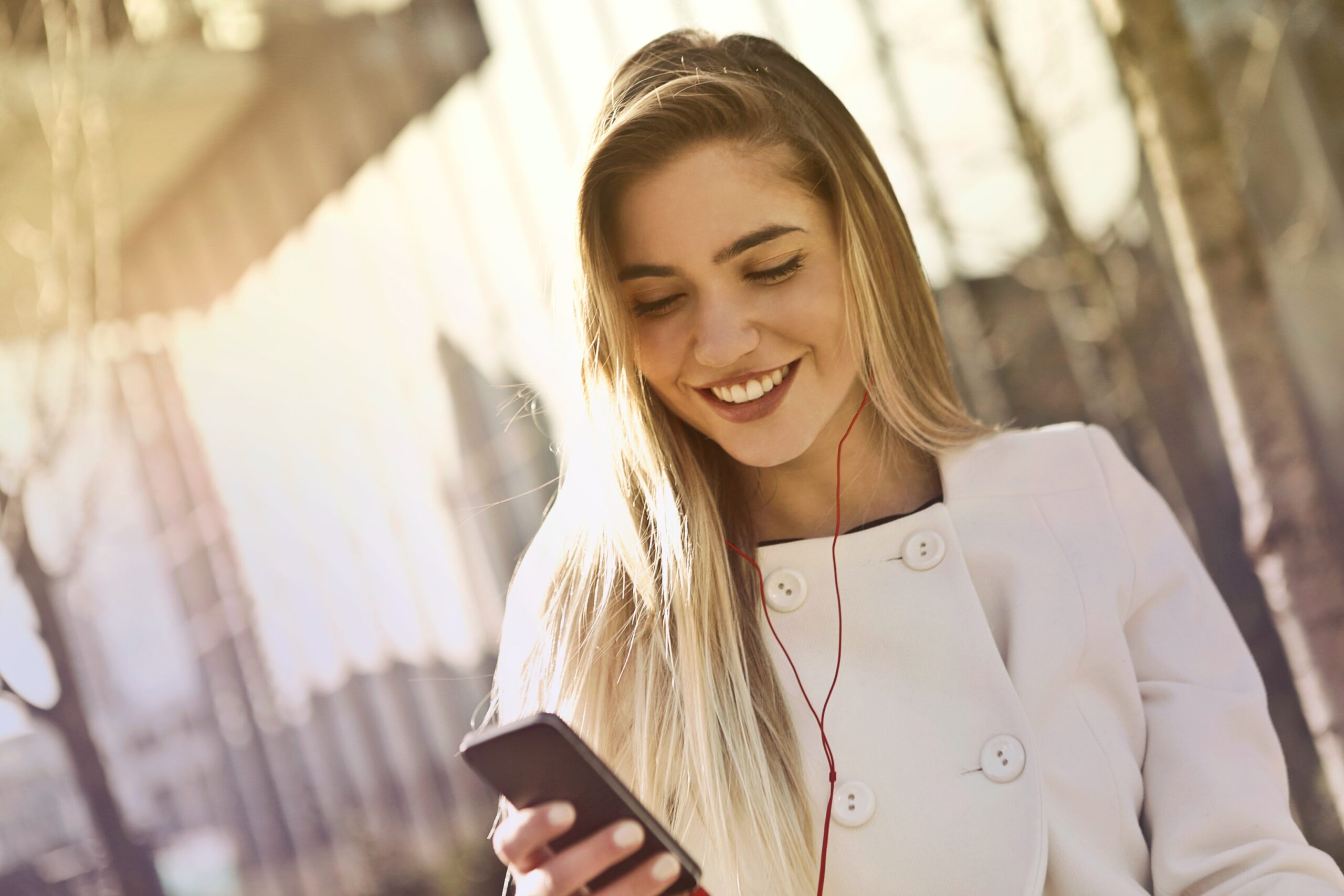 una mujer sonriendo mientras tiene en su mano derecha un móvil y lleva puestos los auriculares
