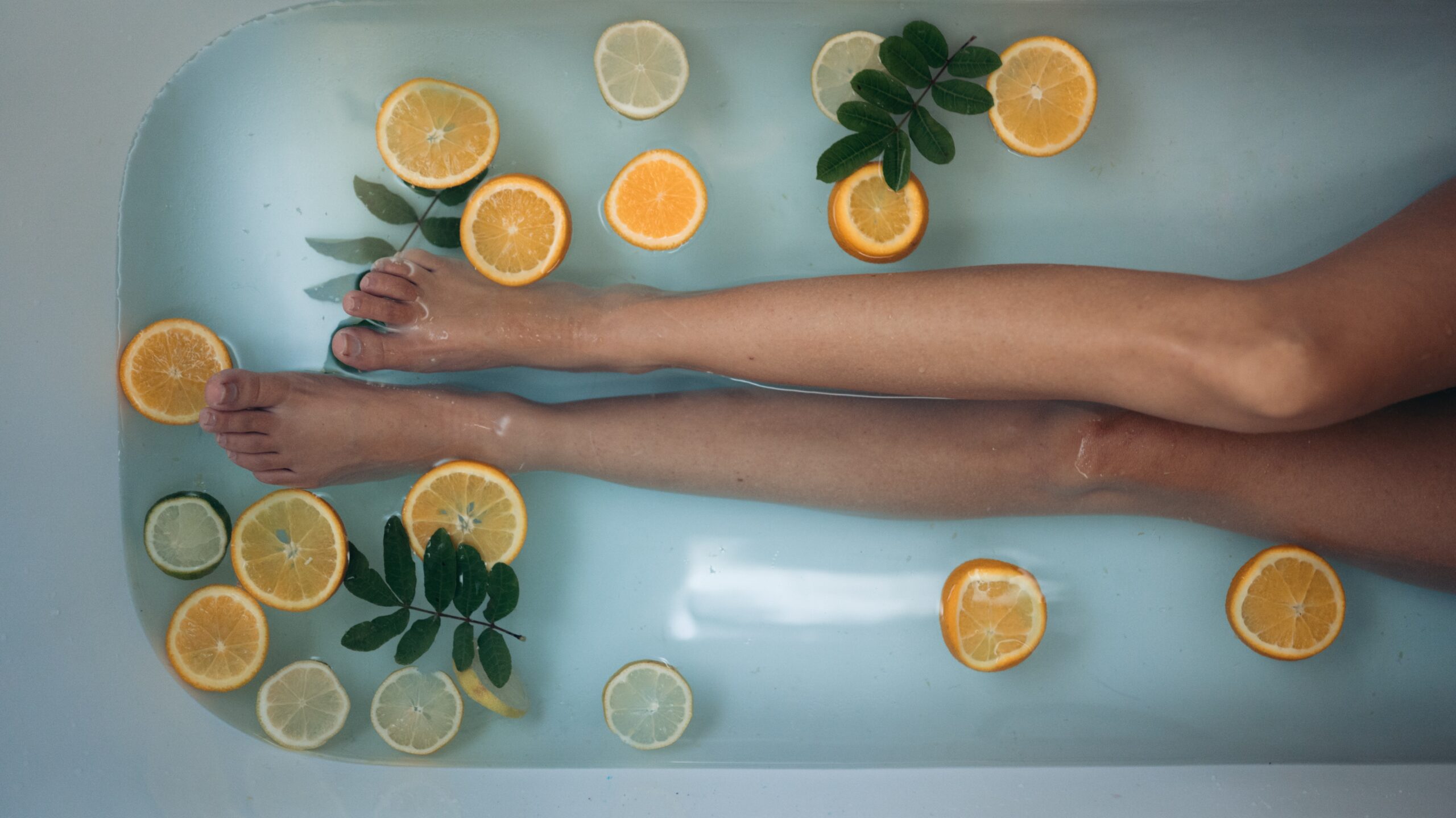 las piernas de una mujer que está en una bañera, el agua tiene rodajas de limones y naranjas
