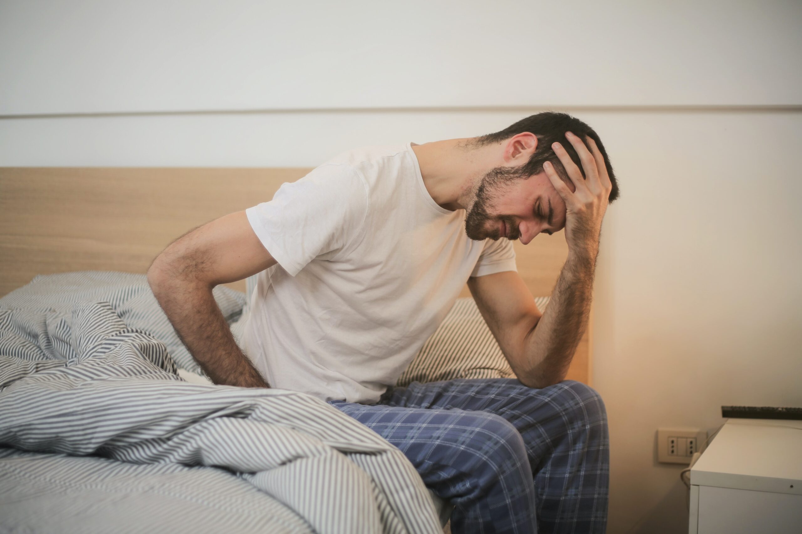 hombre sentado al borde la cama, agarrándose la cabeza