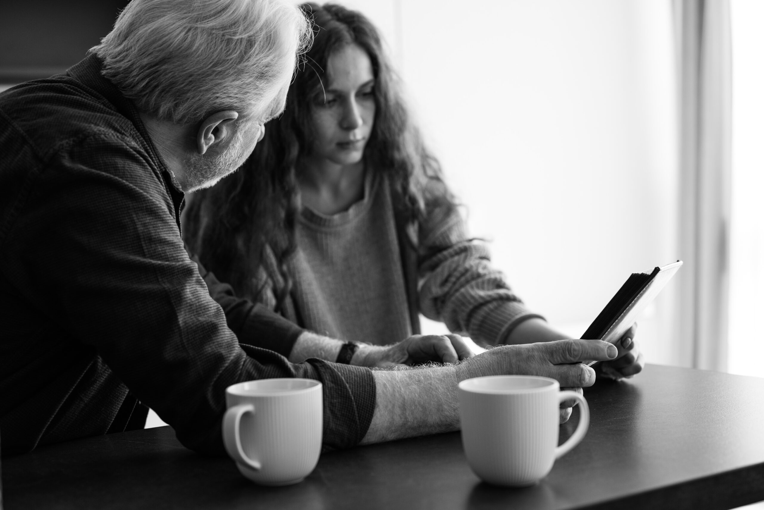 imagen a blanco y negro en la que una mujer le está mostrando algo a un señor mayor desde una tablet