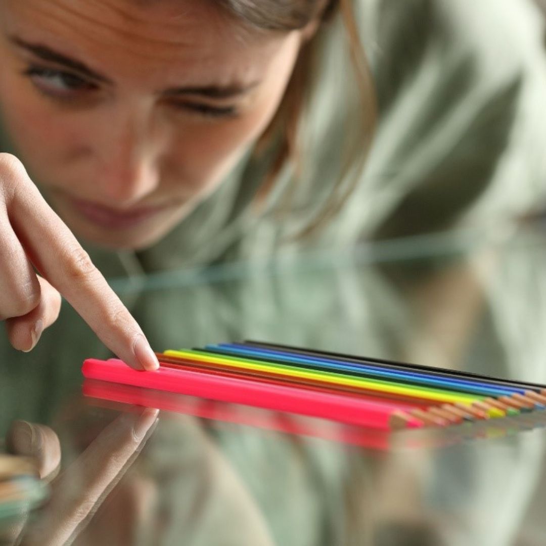 una mujer organizando, contando y apilando lápices de colores de tal manera que la alineación de estos se ve perfecta. Con lo cual, se puede deducir que la mujer tiene un trastorno compulsivo o TOC relacionado al orden y pulcritud de las cosas