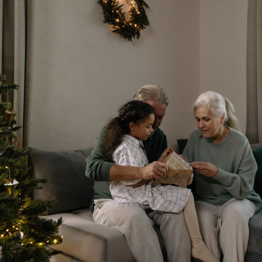 imagen de unos abuelos con posiblemente su nieta, sentados en un sofá, en época de navidad