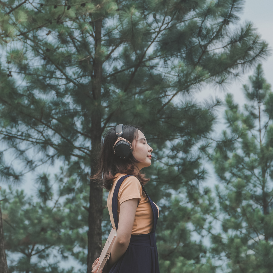 una mujer en medio de la naturaleza, sola, relajada, escuchando música. La imagen hace alusión al efecto positivo de la musicoterapia