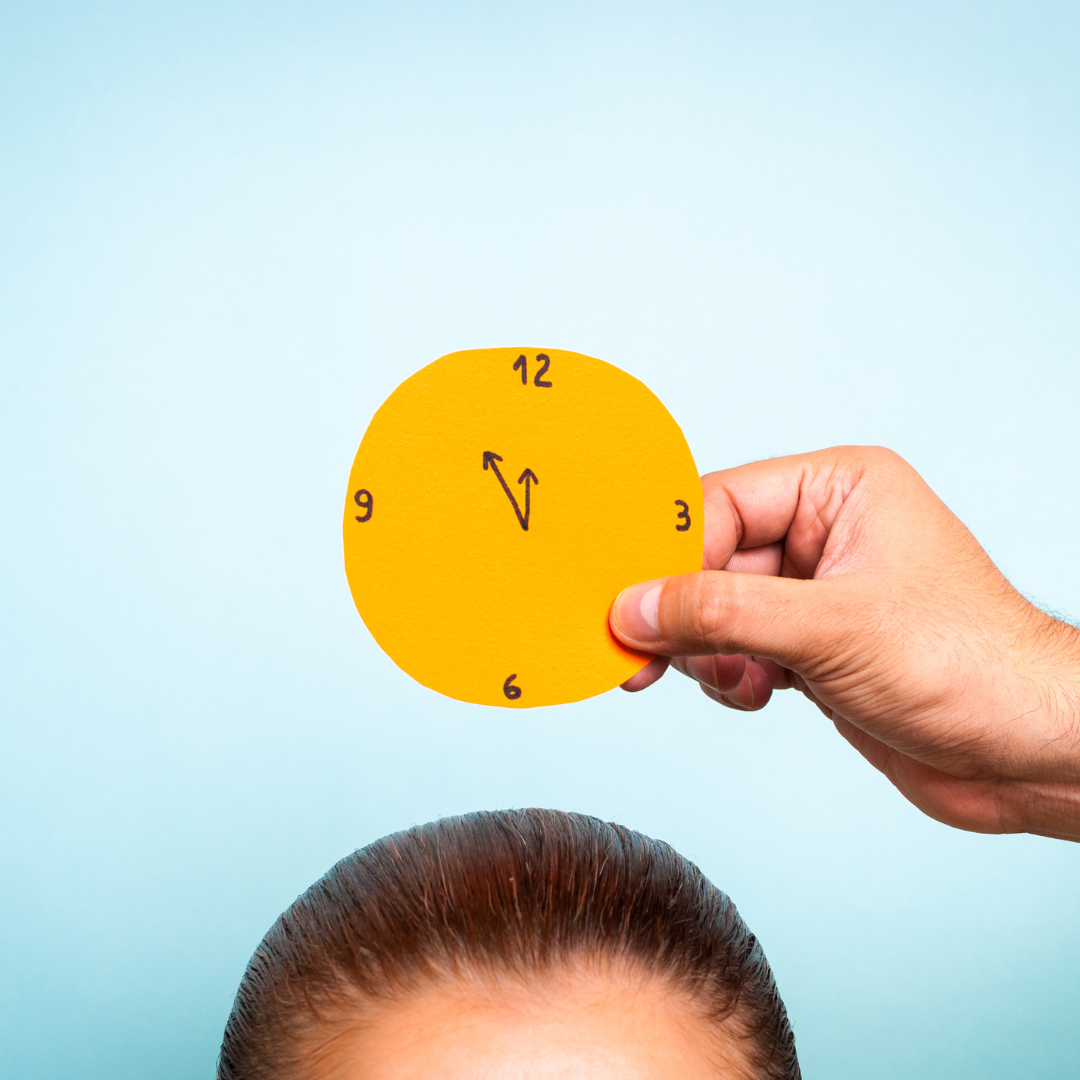 En el centro de la imagen se ve un reloj circular amarillo de papel que es sostenido por la mano de una personas. A su vez, debajo del este, asoma una cabeza que parece de una mujer (solo se ve el cabello y una parte de la frente). La imagen hace referencia a la definición de velocidad de procesamiento