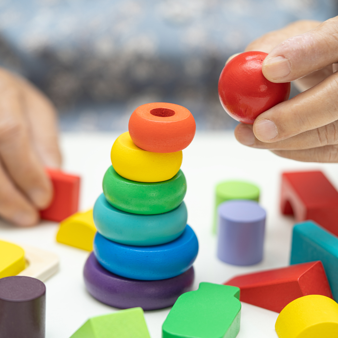 en la imagen se aprecian las manos de una señora mayora que esta sentada frente a una mesa, en la que tiene juegos para crear estructuras, haciendo referencia a un tipo de actividad que se puede realizar para la estimulación en el hogar: cognitiva y (multi)sensorial