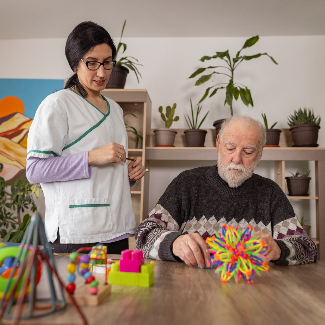 un adulto mayor junto con una terapeuta, realizando ejercicios relacionados con las habilidades motoras y estimulación cognitiva