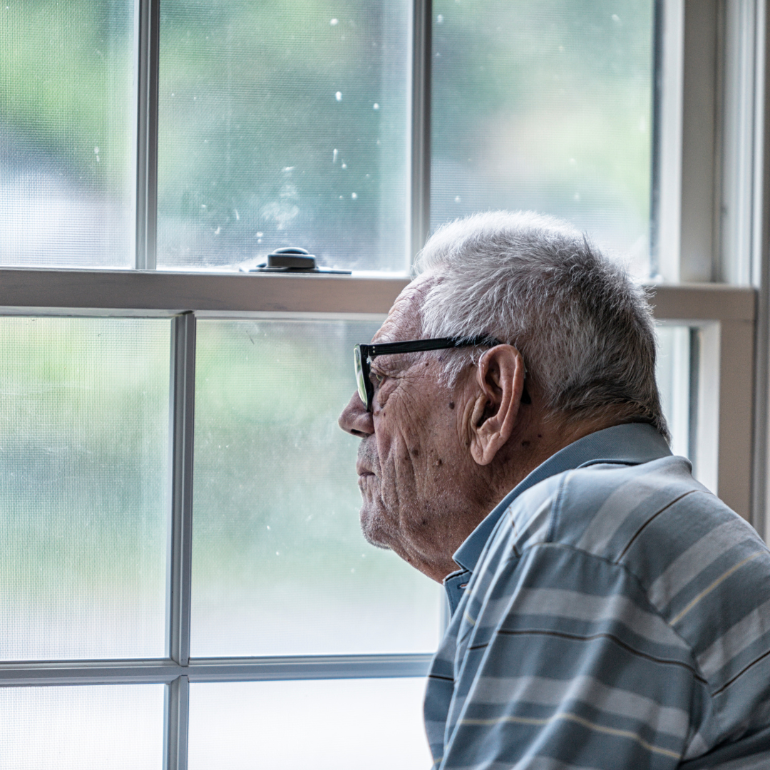 un hombre mayor viendo por una ventana. Imagen que busca hacer referencia a los problemas emocionales y conductuales que pueden llegar a afectar la vida de quienes padezcan trastornos conductuales en demencias