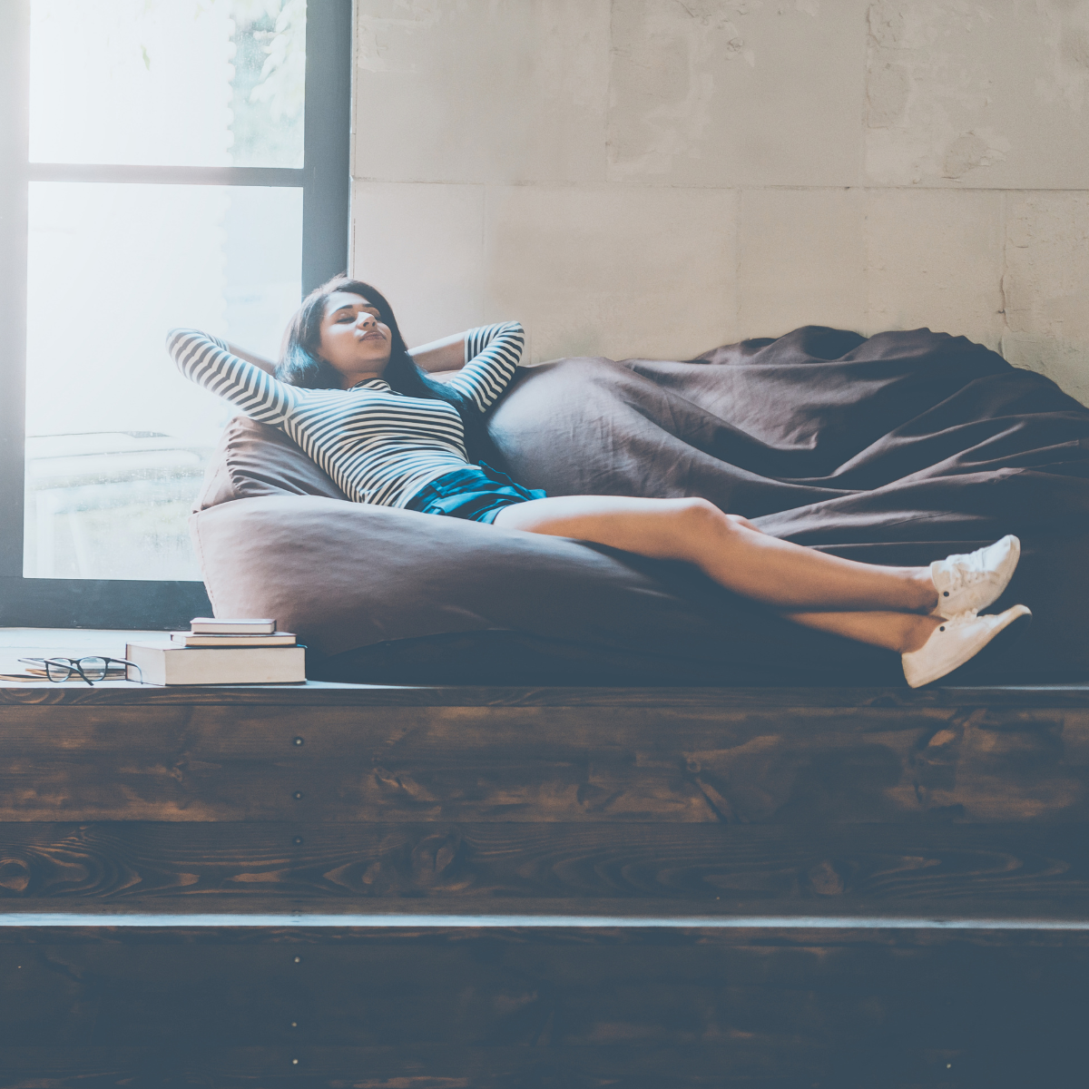 una mujer relajandose, sentada en un puff, en una sala con luces tenues y traqnuila. la imagen busca reflejar uno de los beneficios de gradior multisensorial sobre la ansiedad